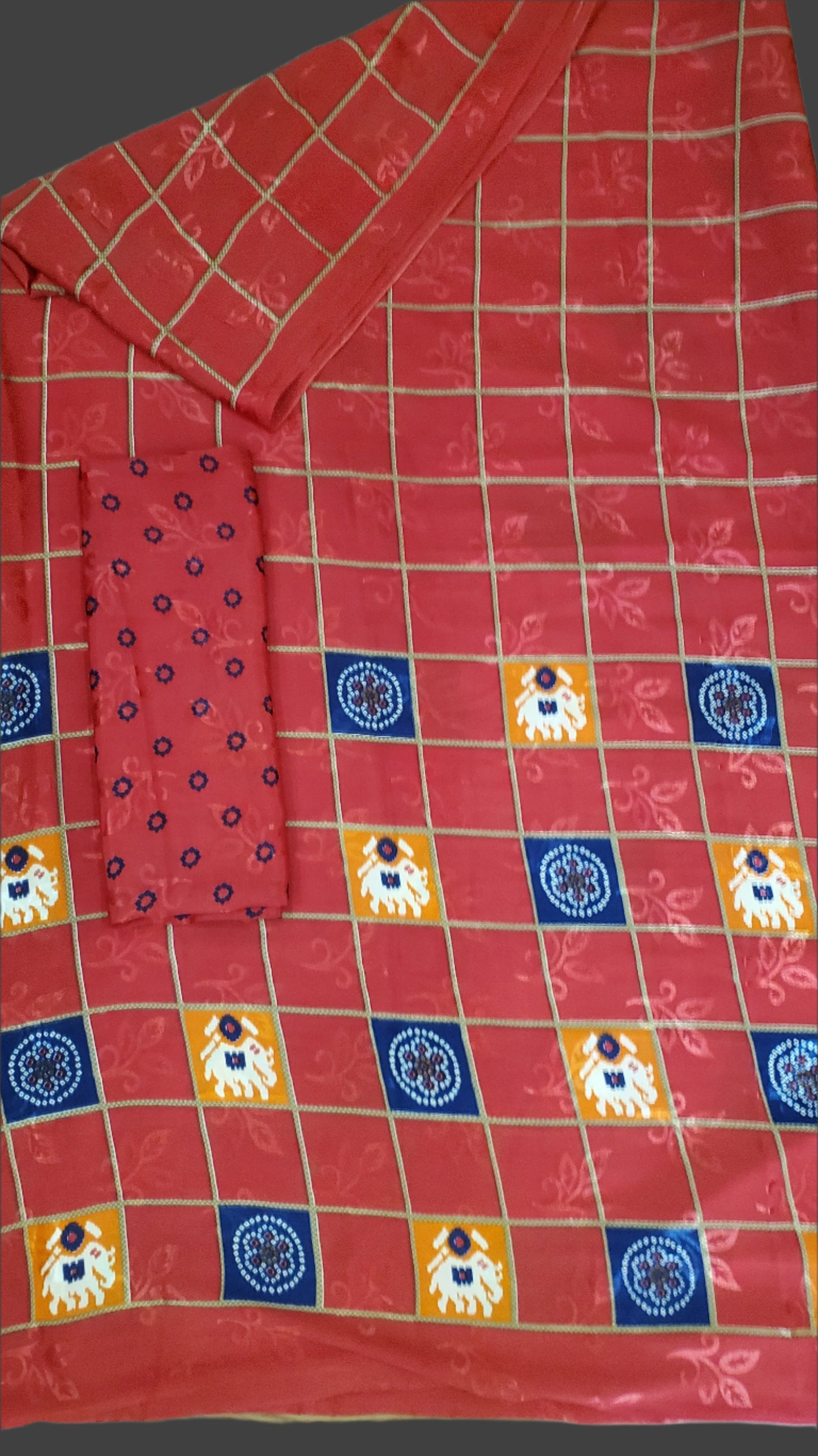 Red fabric with a checkered pattern featuring blue, orange, and white squares on a wooden surface.
