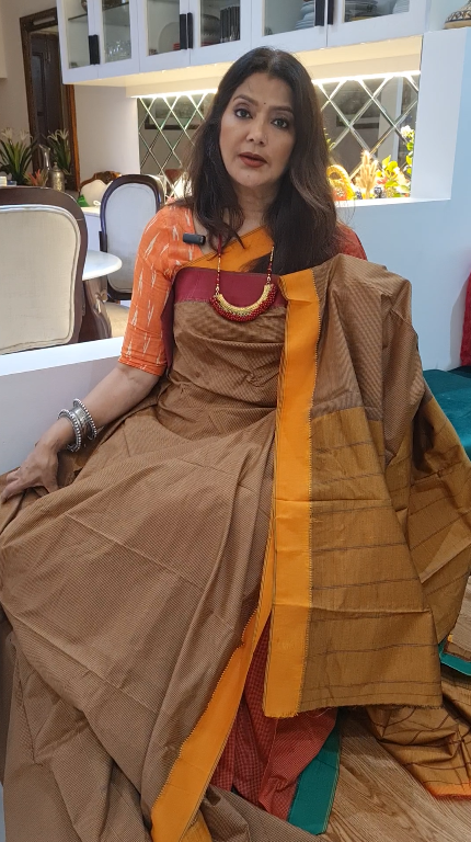 Woman in a traditional outfit with a brown and orange saree in an indoor setting.