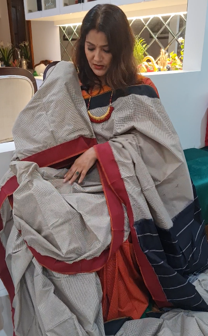 Woman sitting on a couch wrapped in a large beige blanket with red and blue accents.